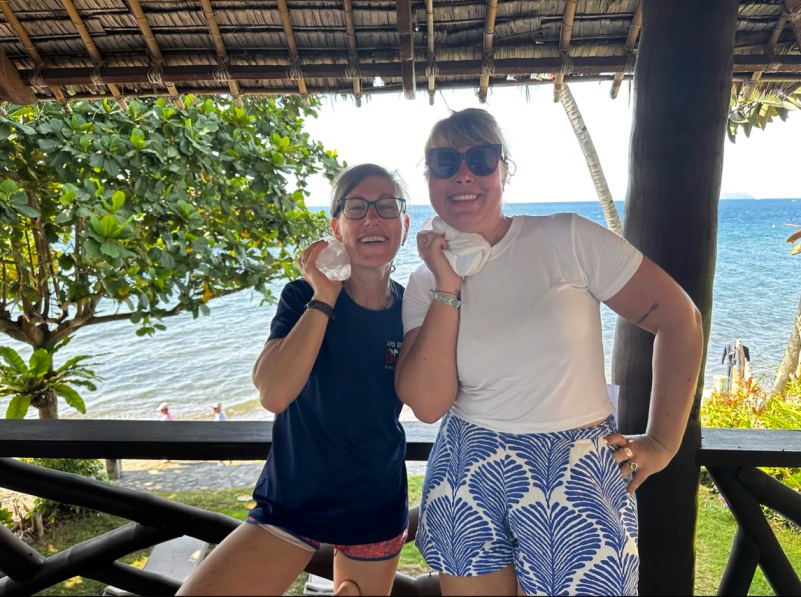 Two women holding ice packs to their skin, laughing on a balcony.