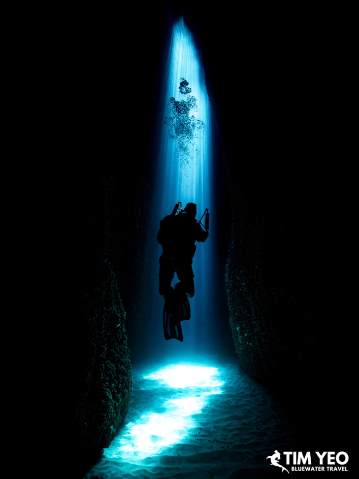 Diver silhouetted in sunbeams inside Leru Cut, Solomon Islands